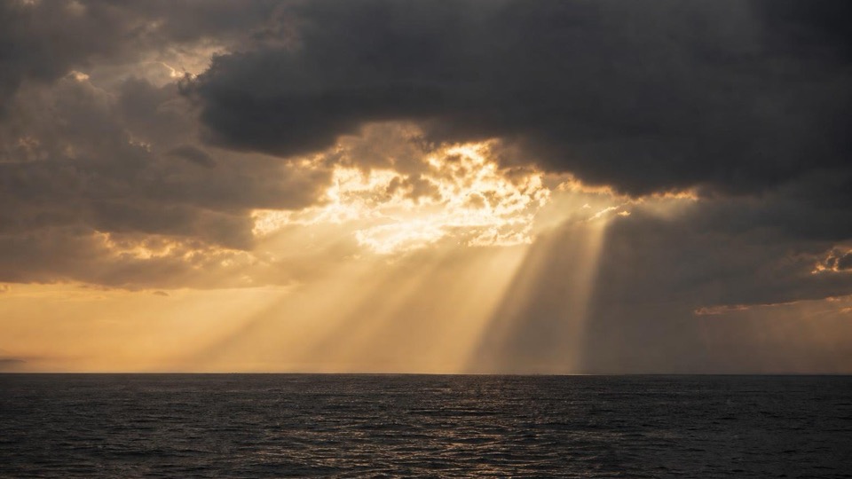 Sunlight breaking through heavy storm clouds over a dark sea